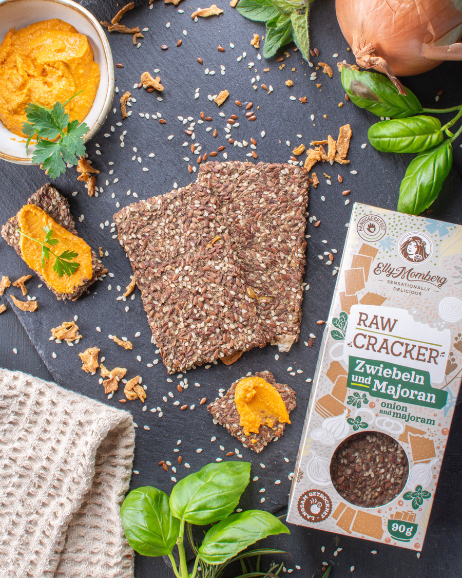 Raw cracker with spices on a dark surface with herbs and a box of crackers.