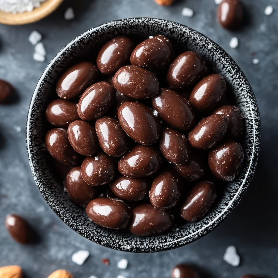 Dark chocolate-covered almonds in a black textured bowl on a dark background