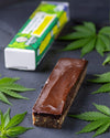 Energieriegel mit Hanfprotein von Elly Momberg mit Hanfblätter und der Orginalverpackung im Hintergrund. 