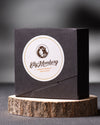 Black box with a circular label featuring a logo and text on a wooden stand with a dark background