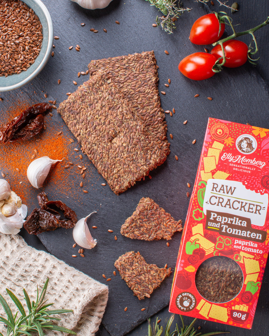 Raw cracker with paprika and tomato flavor on a dark surface with ingredients and packaging.