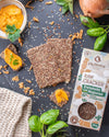 Raw cracker with spices on a dark surface with herbs and a box of crackers.