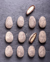 Chocolate covered almonds arranged on a dark surface with one cut open to reveal its interior.