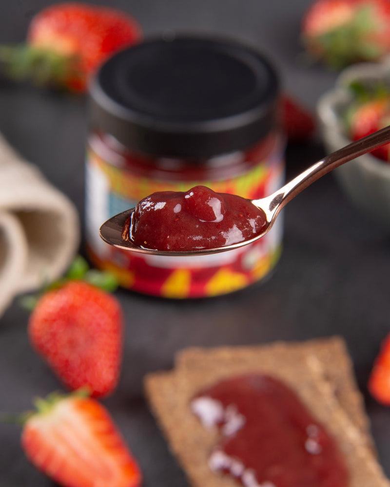 Strawberry jam on a spoon with strawberries and the jam in the background