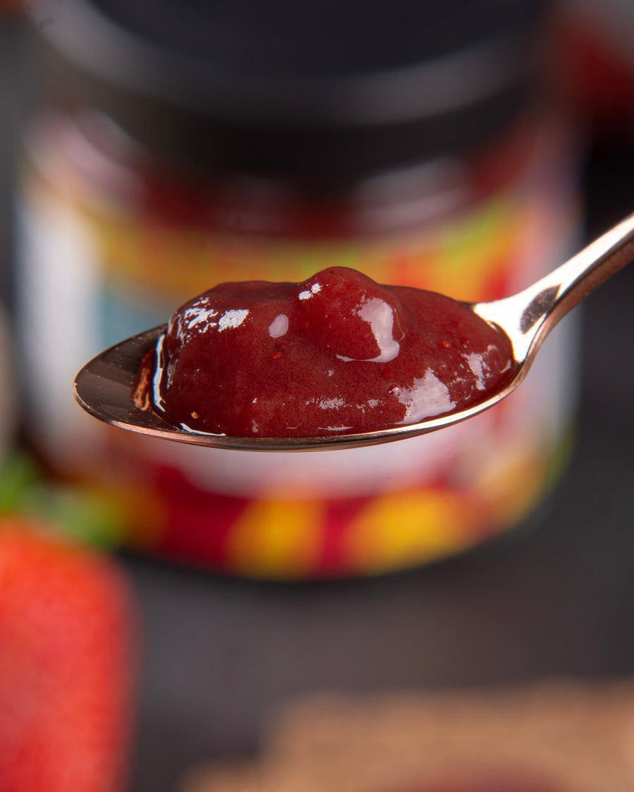 Spoonful of red strawberry jam on a blurred background with a jar and strawberry.
