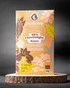 46 %  Schokoladentafel ChocDelight mit Mandeln, ohne Zuckerzusatz und vegan von Elly Momberg, zeigt Verpackung auf Holzuntersetzer