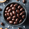 Dark chocolate-covered almonds in a black textured bowl on a dark background