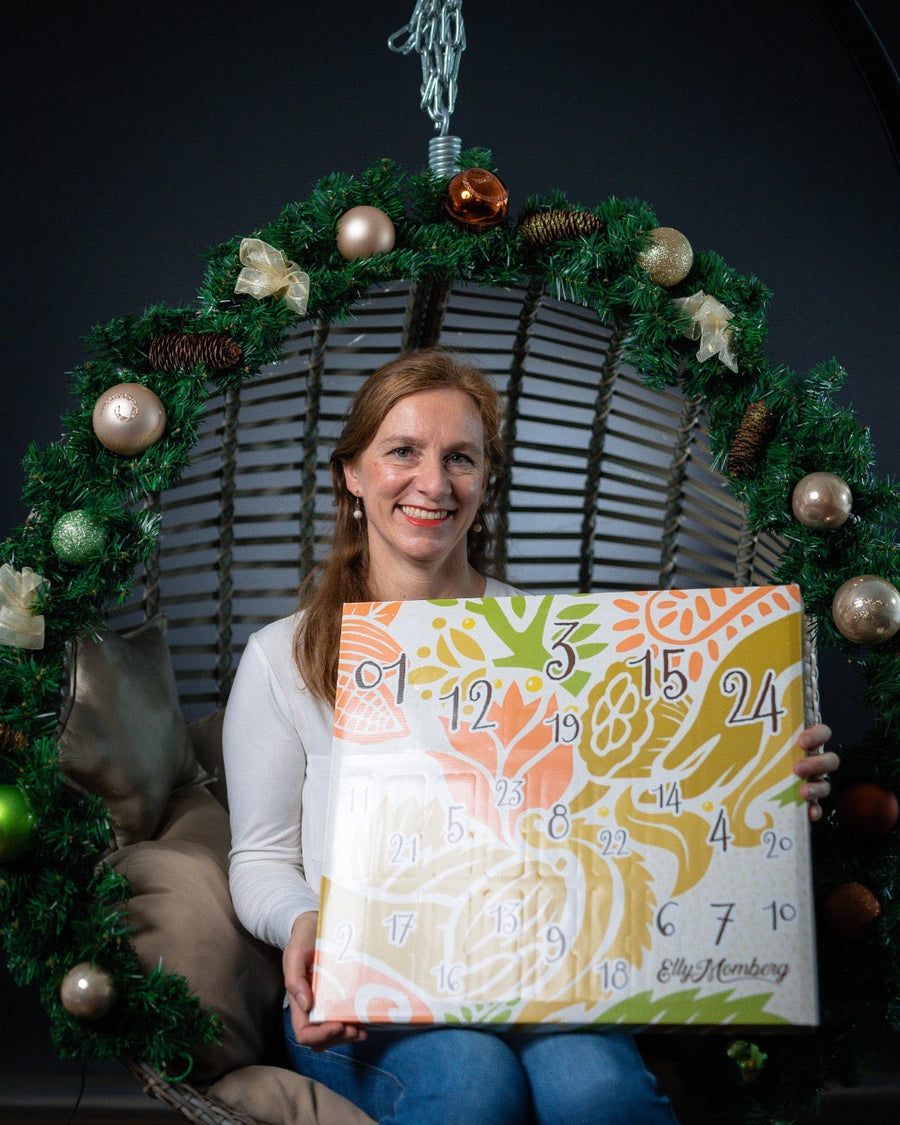 Veganer Adventskalender Deluxe 2026 von Elly Momberg mit 24 Überraschungen ohne Zuckerzusatz, glutenfrei, keto freundlich, und für Diabetiker geeignet Zeigt Gründerin in weihnachtlicher Schaukel mit Adventskalender 
