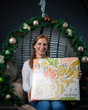 Veganer Adventskalender Deluxe 2026 von Elly Momberg mit 24 Überraschungen ohne Zuckerzusatz, glutenfrei, keto freundlich, und für Diabetiker geeignet Zeigt Gründerin in weihnachtlicher Schaukel mit Adventskalender 